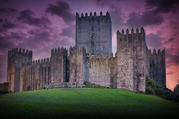 Sunset view of Guimaraes Castle in Portugal, featuring the medieval fortress under a dramatic purple sky during the golden hour.