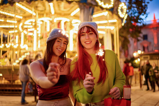 Happy friends celebrating with sparklers at amusement park night