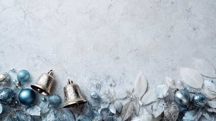 Elegant winter holiday background featuring silver bells, blue and silver ornaments, and frosted foliage on a cool grey textured surface.