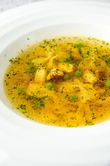 A warm, clear chicken broth soup with bowtie pasta (farfalle), peas, and chopped chicken is served in a modern white bowl on a speckled grey stone surface