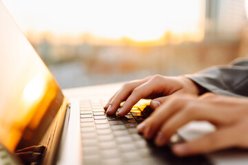 Close-up of hands typing on a laptop in the sunset on a rooftop terrace. A freelancer with a laptop...