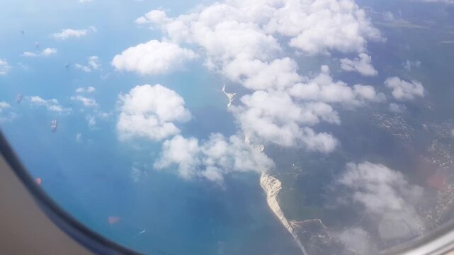 Coastline and ships under clouds window view from airplane over sea