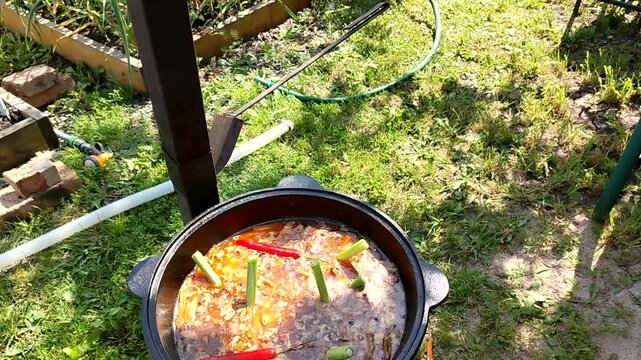 Pilaf cooking in cast iron cauldron outdoors bubbling broth and spices