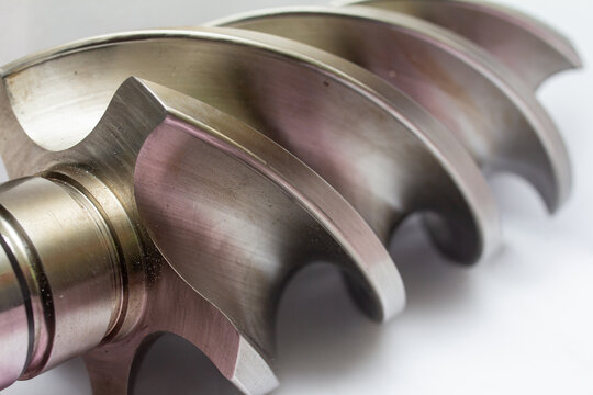 Metallic helical screw rotor from an industrial compressor or gear pump, highlighting the curved lobes, precision machining, and smooth surface finish against a clean white background