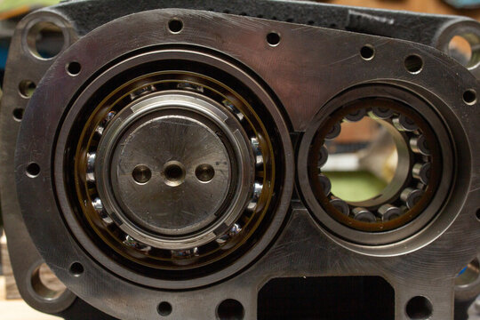 Disassembled industrial compressor or pump housing, revealing two large, precision ball bearings lubricated with oil and mounted in metallic bearing seats for rotor support