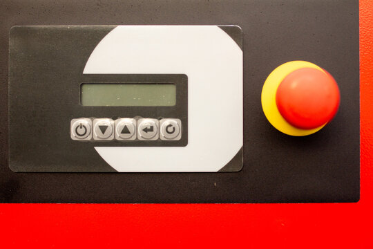 Industrial machine control panel featuring a digital display, functional buttons, and a prominent red/yellow emergency stop button for safety and automation concepts - Powered by Adobe