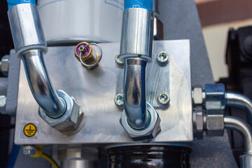 Shiny chrome hydraulic/pneumatic pipe fittings and steel bolts attached to a heavy, machined metallic manifold block, emphasizing fluid power systems and industrial quality