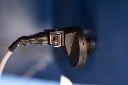 A sealed industrial sensor or electrical connector plugged into a dark blue machine panel, highlighting the safety clip and protective casing for electronic control systems