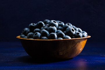 Fresh Blueberries in a wooden bowl on a blue wooden table with blue backdrop.