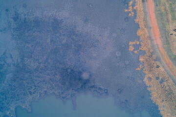 Aerial top down view of cracked blue mud texture near red dirt road. Dry industrial waste pattern...
