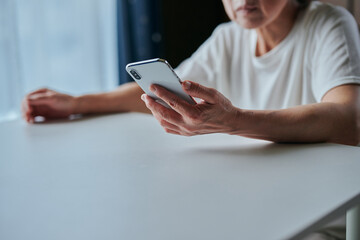 部屋でスマホを操作するシニア女性