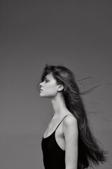 Fototapeta premium Black and white profile of a young woman with long flowing hair in a black dress against a plain gray background