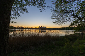 A panoramic, symmetrical shot of Moritzburg Castle at twilight. The sky transitions from a deep blue at the top to an intense orange at the horizon