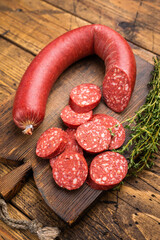 Sliced and whole Turkish sucuk (sujuk) on a rustic cutting board with thyme. Spicy dry-cured sausage, top view.