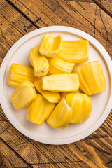 Sweet, golden yellow jackfruit pods (bulbs) served on a white plate on a rustic wooden table. Fresh, tropical fruit snack. © Mironov