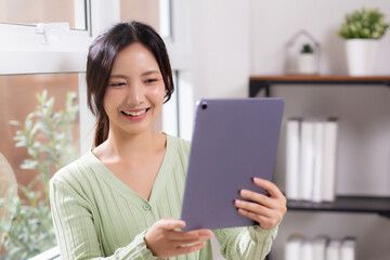 Portrait young asian business woman using digital tablet computer for video call by the window in living room at home office, businesswoman and expression while video call, lifestyle and business.