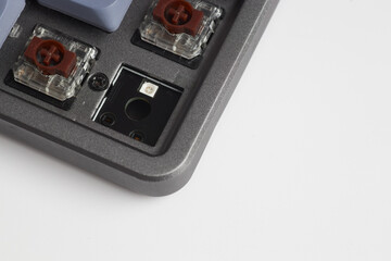 Close-up of mechanical keyboard corner with one switch removed, revealing RGB socket and brown tactile switches
