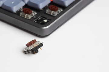 Mechanical keyboard with a removed brown switch placed on white surface, showing socket and switch details
