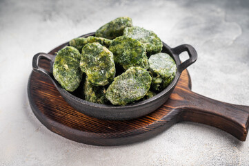 Overhead shot of frozen spinach blocks in a cast iron skillet on a wooden board. Grey textured background with copy space.