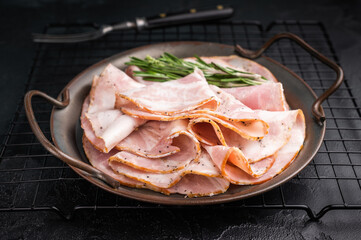 Slices of Italian Pancetta Arrotolata with rosemary in a metal dish, next to a vintage fork on a dark background with copy space.