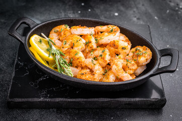 Grilled shrimps prawns in a cast iron skillet on a black slate surface. Elegant, moody, and rustic photo with large negative space for text.