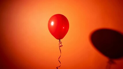 Red balloon floating gracefully with dynamic shadow play against orange background