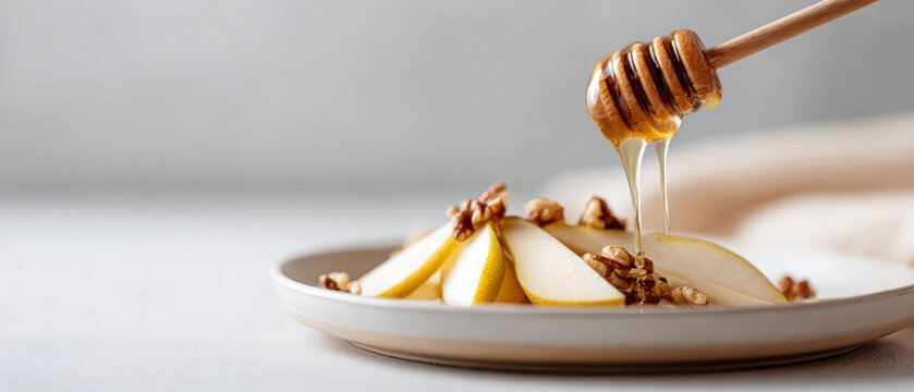Close-up of honey dripping from wooden dipper onto sliced pears with walnuts on white plate in soft natural light