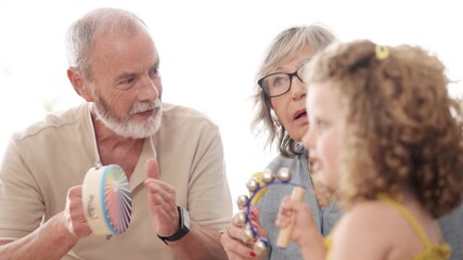 Happy grandparents having fun with their little granddaughter, playing musical instruments and singing together. A joyful family moment