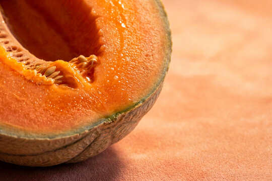 Charentais Melon Slice Showing Deep Orange Flesh and Seed Cavity on Warm Peachy Background