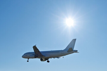 Obraz premium White Passenger Airplane Flying in Clear Blue Sky with Bright Sun Flare