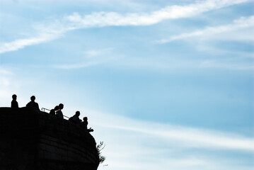 Schwarze Silhouetten von unkenntlichen Touristen auf Burgturm auf Burg Hohenneuffen vor blauem Himmel mit Schleierwolken