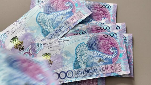 A close-up of ten thousand Kazakhstani tenge banknotes with an image of a snow leopard falling one by one onto the table