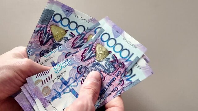 Close-up of a man's hands counting a stack of ten thousand Kazakhstani tenge banknotes