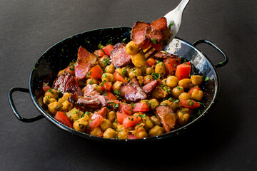 Rustic Mediterranean Chickpeas and Smoked Meat Stew with Diced Tomatoes and Parsley in a Black Skillet