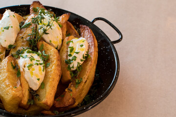 Rustic Fried Potato Wedges with Creamy Cheese Topping, Fresh Thyme, Chives, and Olive Oil in a Black Skillet