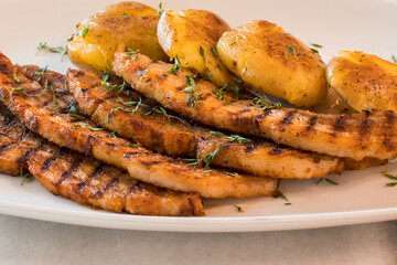 Close-up of Sliced Grilled Pork Chops with Crispy Smashed Potatoes and Fresh Thyme Garnish