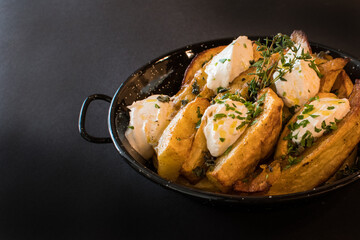 Rustic Fried Potato Wedges with Creamy Cheese Topping, Fresh Thyme, Chives, and Olive Oil in a Black Skillet