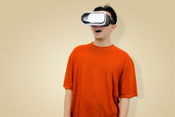 young Asian man in an orange t-shirt wearing a virtual reality headset, symbolizing immersive entertainment in studio background