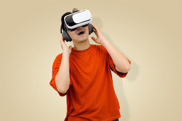 Excited young Asian man in an orange t-shirt wearing a virtual reality headset, symbolizing immersive entertainment or controlling the sound of the metaverse in studio background