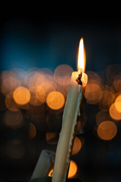 Vela encendida en la oscuridad con dram&aacute;tico bokeh de luces c&aacute;lidas de fondo