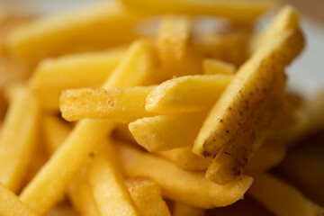 Extreme close-up of golden, crispy French fries. An appetizing pile of this popular fast food snack creates a delicious, textured background with selective focus.