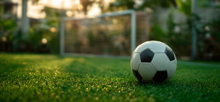 white soccer ball rests prominently on freshly mown green field, with the goal and net visible in background - Powered by Adobe
