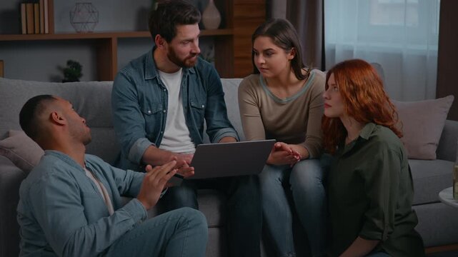 Multiracial four friends with laptop on couch in coworking working online talking multiracial people men women discussing looking computer at home party diversity buddies browsing pc in living room