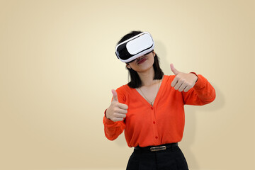 Happy young Asian woman in an orange t-shirt wearing a VR headset and giving a double thumbs-up gesture, symbolizing approval, excellent experience studio background