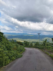 An aerial perspective of vibrant green hillside forests stretching toward mist-covered mountains, forming a peaceful and calming landscape in Bandarban, Chittagong Division, Bangladesh.