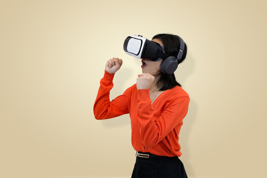 young Asian woman in an orange sweater wearing a virtual reality headset and headphones, symbolizing amazement or surprised within an immersive virtual environment in studio background - Powered by Adobe