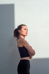 Confident sporty woman outdoors striking pose against white wall, strong posture