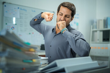 Tired businessman yawning late at night, struggling with insomnia and the pressures of work,...
