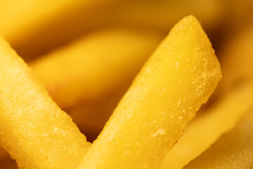 Macro close-up of golden frozen french fries. Detailed texture of raw potato sticks ready for cooking. An ideal background for fast food and semi-finished products.