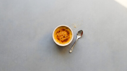 Minimal cr&egrave;me br&ucirc;l&eacute;e dessert with caramel top and spoon on a clean gray background.